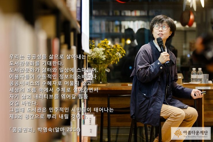 마이크를 들고 의자에 앉아 스크린을 보며 강연을 하고 있는 박영숙 관장