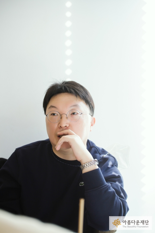 우리 모두가 공정한 시작을 할 수 있는 사회가 되길 바라는 마음으로 아름다운재단 교육영역에 기부하겠다는 말을 하고 있는 정경찬 기부자. 하얀 얼굴에 샤프한 눈매를 가지고 있으며 손을 턱에 올린채 이야기 중이다. 