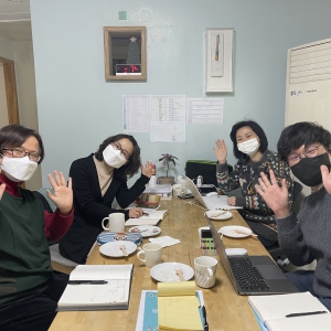 사무작의 사무실 책상 앞에 마스크를 쓰고 앉아 모두 양 손을 펼치며 카메라를 바라보고 있다.