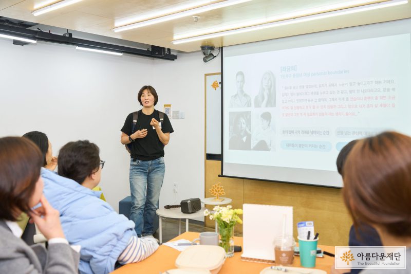 한 사람이 발표하고 있고, 청중들이 경청하고 있는 사진 