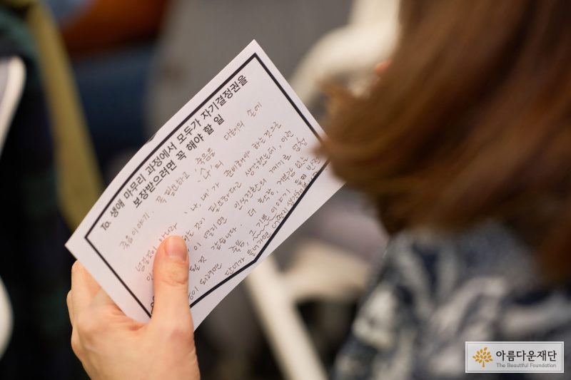 왼손으로 종이를 들고 있는 사진. 종이에는 생애 마무리 과정에서 모두가 자기결정권을 보장받으려면 꼭 해야할 일 이라고 적혀 있고, 그 아래 참가자가 적어준 응원 글이 적혀 있다. 