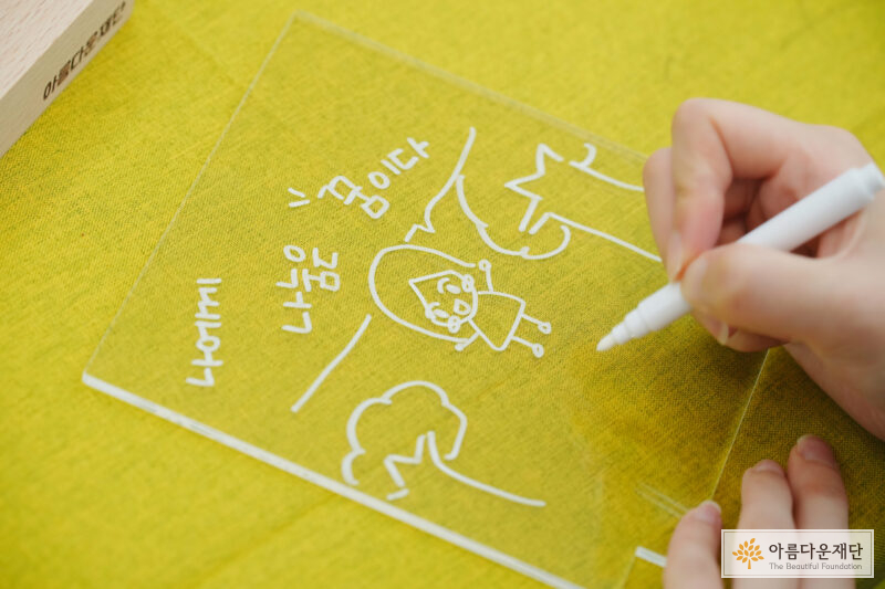 기부회원님이 아크릴 무드등 DIY 체험을 하고 있는 모습. 아크릴 판에 '나에게 나눔은 꿈이다' 라는 문구와 그림이 그려져 있음